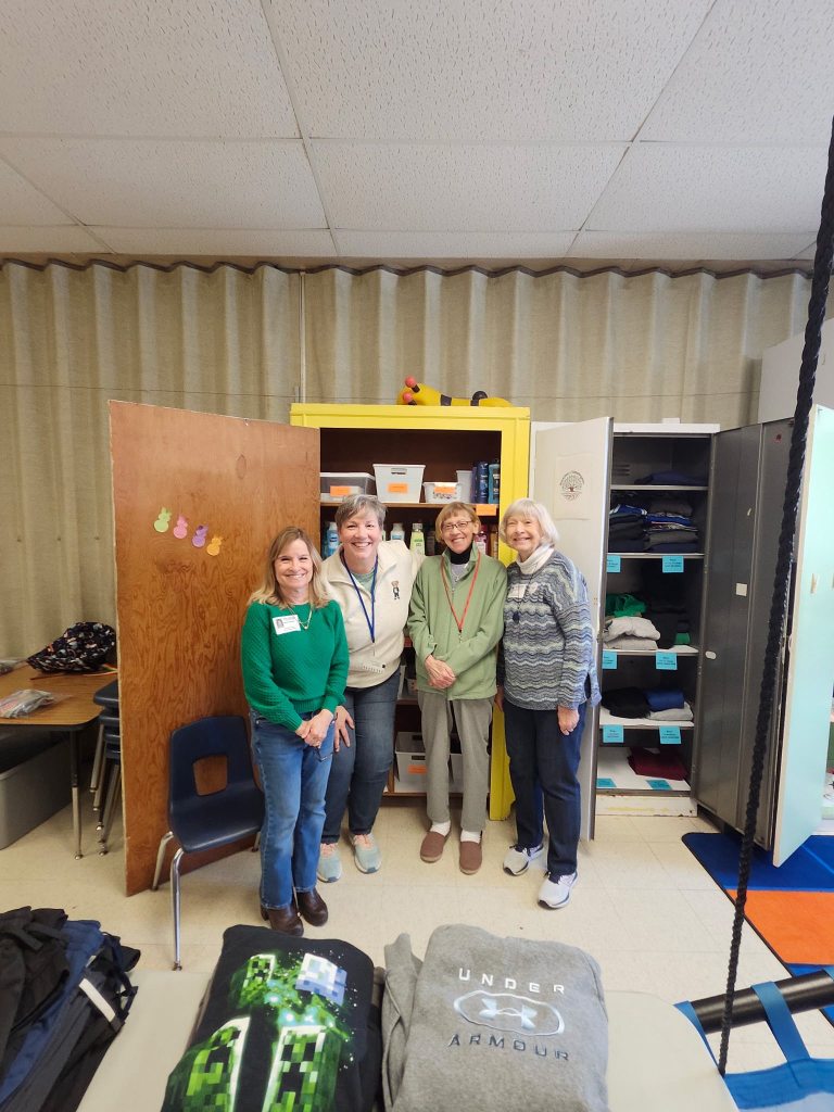 four volunteers standing in front of open cabinets full of hygiene supplies and clothing.