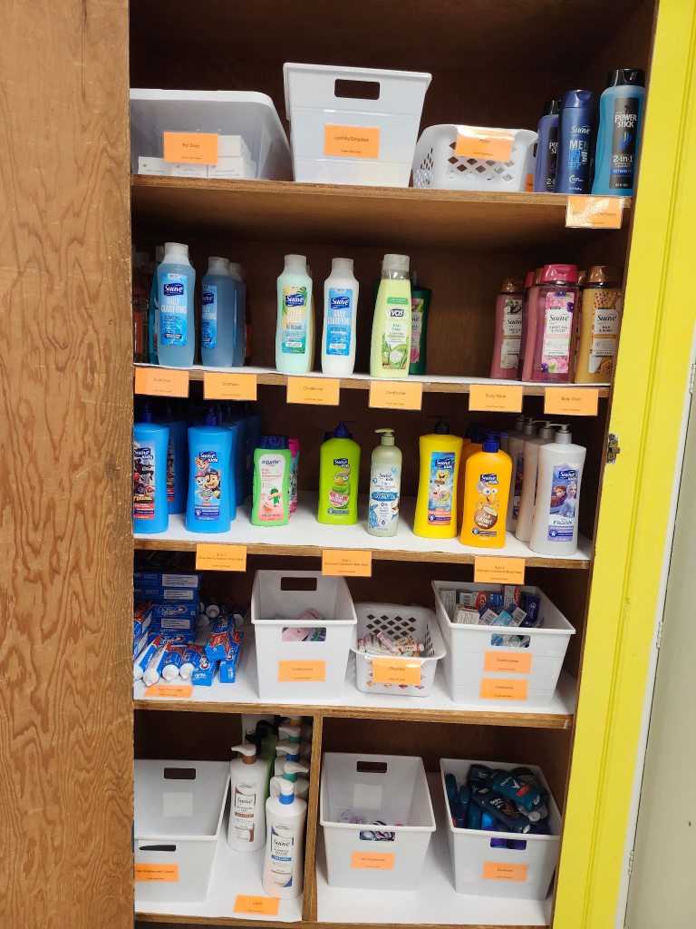 A cabinet neatly stocked with shampoo, body wash, toothbrushes/paste, hand lotion, deodorant and lip balm.